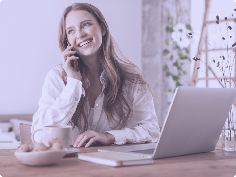 Lächelnde Mitarbeiterin telefoniert vor dem Laptop – mobiles Arbeiten verbindet Flexibilität und gute Erreichbarkeit.